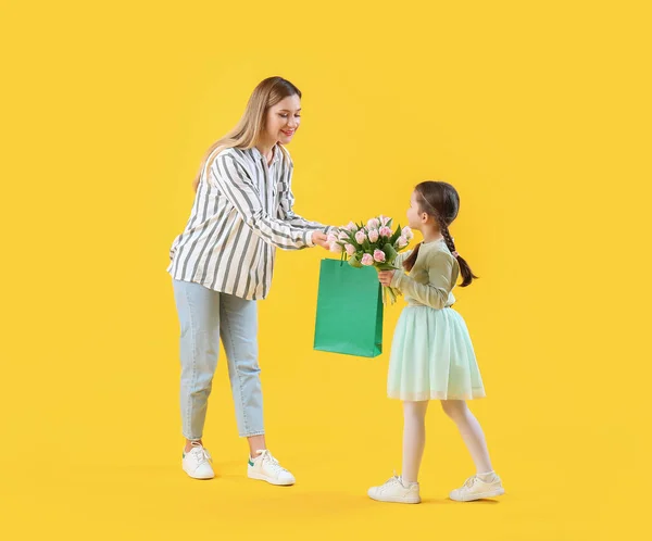 stock image Cute little girl greeting her mother with tulips and gift bag on yellow background