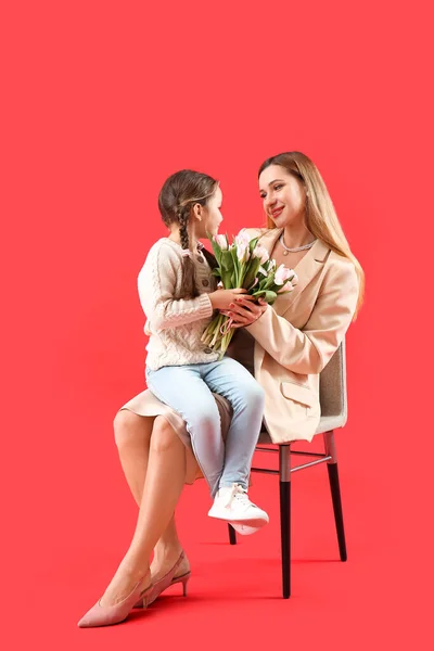 stock image Cute little girl greeting her mother with tulips on red background