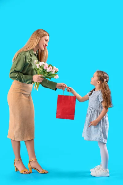 stock image Cute little girl greeting her mother with tulips and bag on blue background