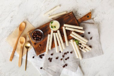 Board with delicious wafer rolls, coffee beans and condensed milk on white grunge background