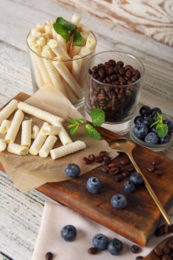 Beyaz ahşap arka planda lezzetli gofret, yabanmersini ve kahve çekirdekleri olan bir pano.