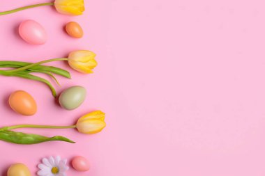 Pembe arka planda boyanmış Paskalya yumurtaları ve bahar çiçekleriyle kompozisyon