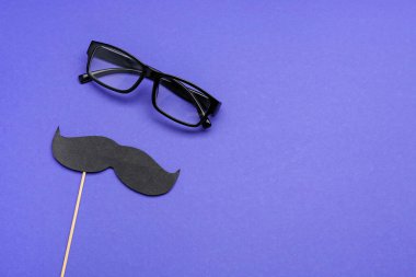 Kağıt bıyıklı tahta sopa ve mavi arka planda gözlük.