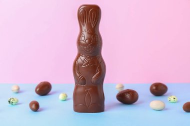 Masada pembe arka planda yumurtaları olan çikolatalı Paskalya tavşanı.