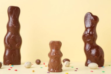 Sarı arka planda yumurta ve çikolata parçacıkları olan Paskalya tavşanları.