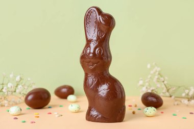 Yeşil arka planda yumurta ve çiçeklerle çikolatalı Paskalya tavşanı