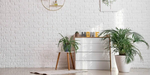 Chest of drawers with houseplants near white brick wall in room
