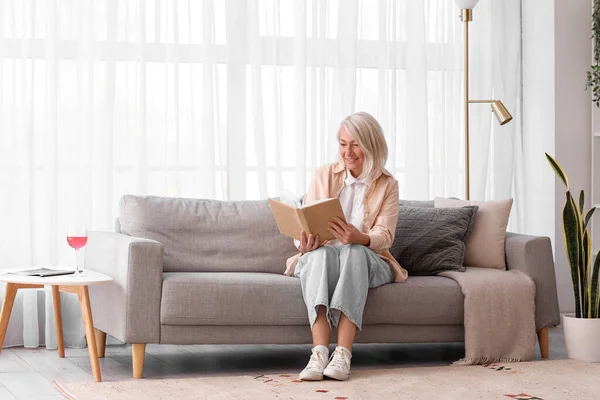 Mature Woman Reading Book Grey Sofa Home — Stock Photo, Image