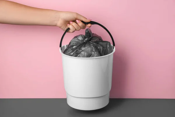 Woman with rubbish bin near pink wall