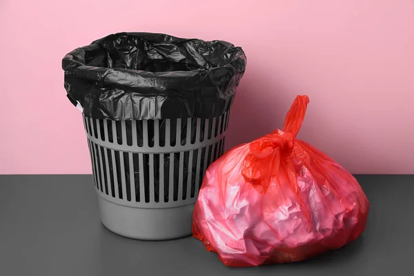Rubbish bin and bag with garbage near pink wall