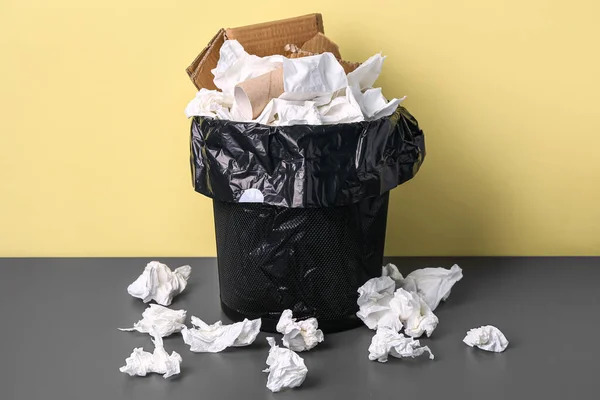 Rubbish bin with paper garbage near yellow wall