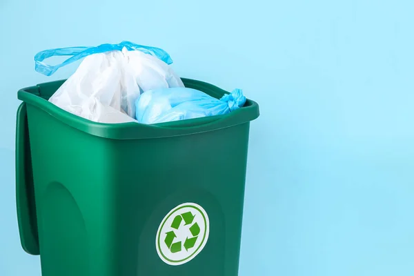 Recycle bin with garbage bags on blue background, closeup