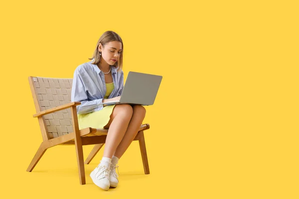 Mujer Joven Usando Portátil Sillón Madera Sobre Fondo Amarillo — Foto de Stock