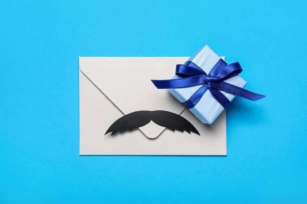 Envelope with paper mustache and gift for Father\'s Day celebration on color background