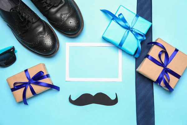 Composition with paper frame, mustache, male shoes and gifts for Father\'s Day celebration on color background