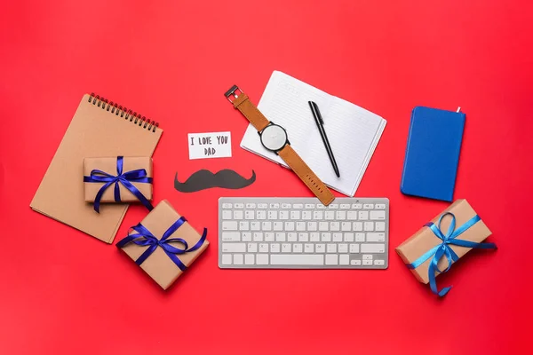 Composition with keyboard, wristwatch, stationery and gifts for Father\'s Day celebration on red background
