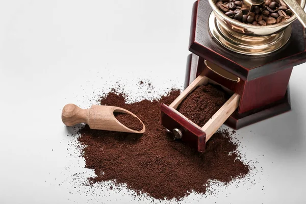 Coffee grinder with powder and scoop on white background
