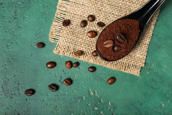 Spoon of coffee powder with beans on green table, closeup
