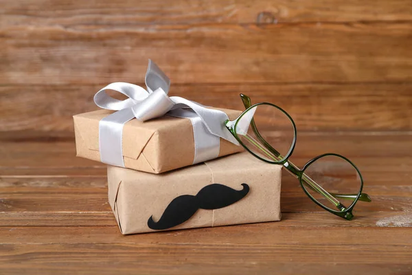 Gifts with paper mustache and eyeglasses on wooden background. Father\'s Day celebration