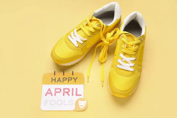 stock image Paper with text HAPPY APRIL FOOLS and sneakers on yellow background