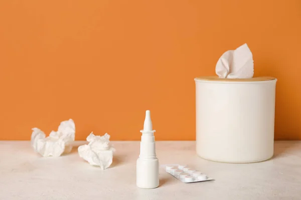 Nasal drops with pills and tissue box on table near orange wall. Allergy concept