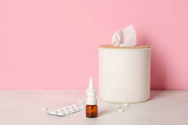 Nasal drops with pills and tissue box on table near pink wall. Allergy concept