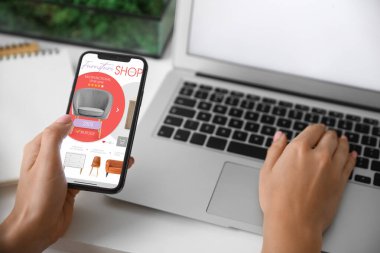 Cep telefonu ve dizüstü bilgisayarı olan bir kadın yeni mobilya alıyor.
