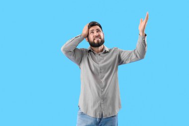 Young man suffering from loud noise on blue background