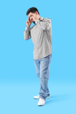 Young man suffering from loud noise on blue background