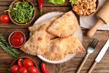 Ahşap zemin üzerinde pişmiş et, et, sebze, sos ve otlarla dolu tabaklar.