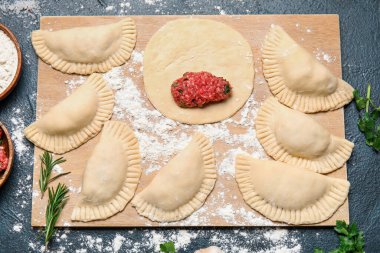 Koyu arka planda çiğ et börekleri olan ahşap tahta, yakın plan.