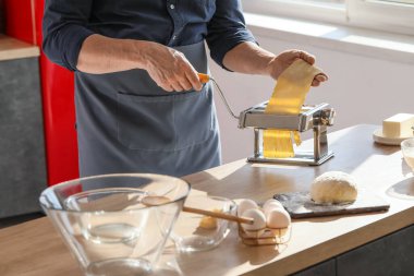 Adam mutfaktaki masada makineyle makarna yapıyor, yakın plan.