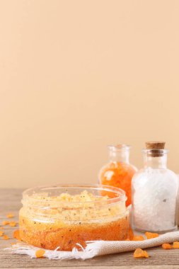 Vücut fırçası kavanozu ve deniz tuzu şişeleri renkli duvarın yanındaki ahşap masada.