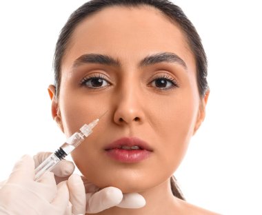 Genç bir kadın, beyaz arka planda yüzüne enjeksiyon yaptırıyor.