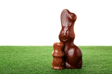 Beyaz arka plana karşı yeşil çimlerde çikolatalı Paskalya tavşanları