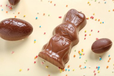 Çikolatalı Paskalya tavşanı, bej arka planda yumurta ve çikolata parçacıkları, yakın plan.