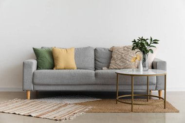 Yastıklı rahat gri kanepe ve ışık duvarının yanındaki masada vazoya ağaç dalları.