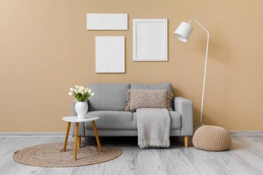 Yastıklı rahat gri kanepe ve bej duvarın yanındaki masada lale çiçeği vazosu.