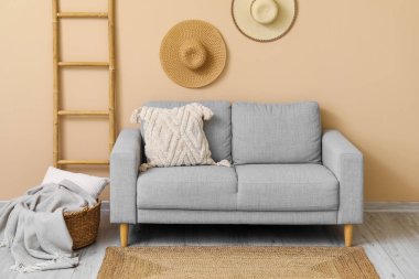 Yastıklı rahat gri kanepe, sepetli ekose, merdiven ve bej duvarın yanında asılı şapkalar.