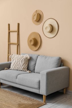 Yastığı, merdiveni ve bej duvarın yanında asılı şapkası olan rahat gri kanepe.