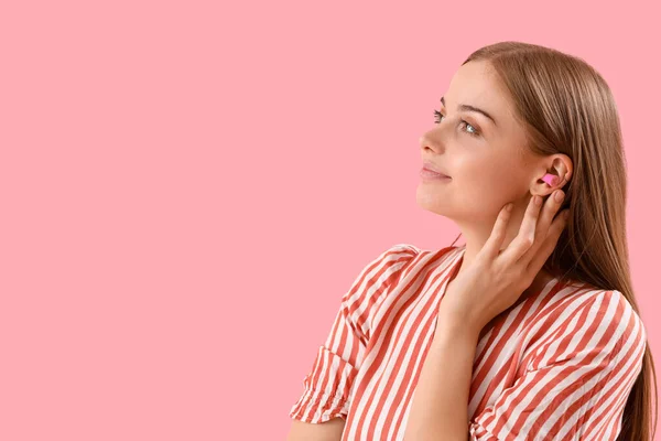 Young woman with ear plugs on pink background, closeup