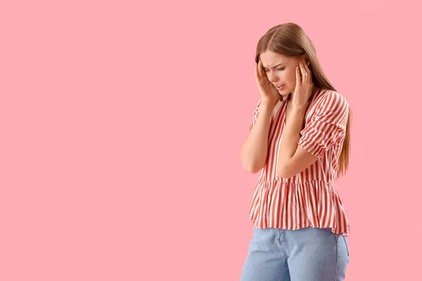 Young woman suffering from loud noise on pink background