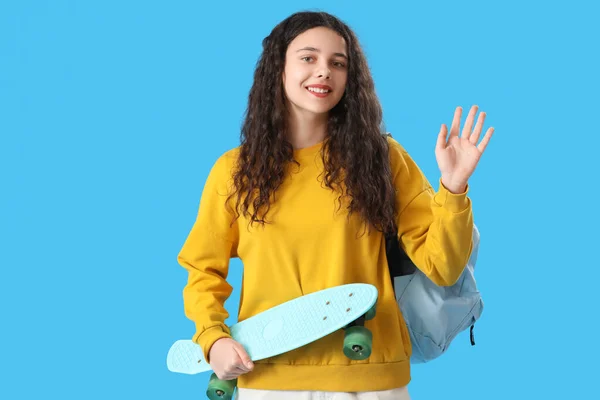 Tonårstjej Med Skateboard Och Ryggsäck Viftande Hand Blå Bakgrund — Stockfoto