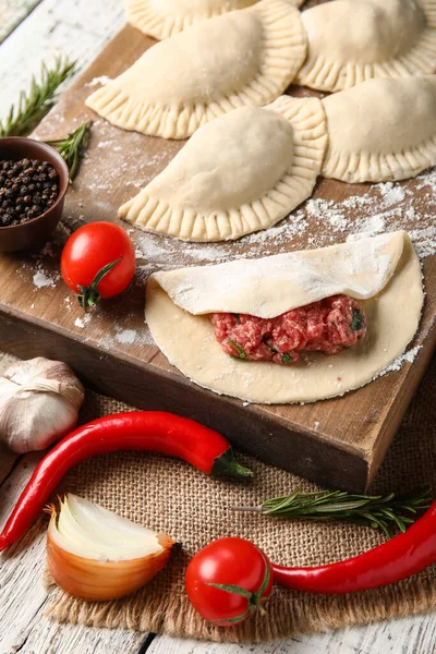 stock image Board with raw meat empanadas and ingredients on light wooden background, closeup