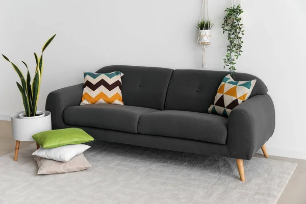 靠近白墙的舒适的黑色沙发 靠垫和室内盆栽 — 图库照片