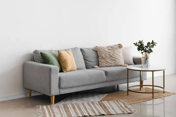 舒适的灰色沙发 靠轻墙的桌上放有靠垫和植物枝条的花瓶 — 图库照片