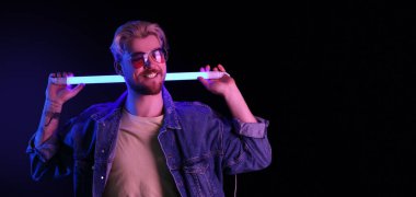 Koyu arkaplanda neon lambası olan yakışıklı genç adamın tonlu portresi.