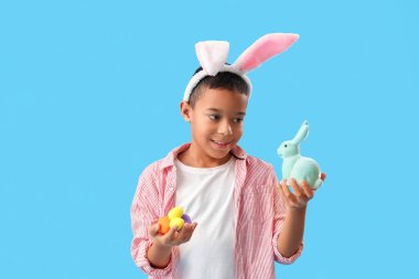 Mavi arka planda Paskalya yumurtası ve tavşanı olan küçük Afro-Amerikalı çocuk.