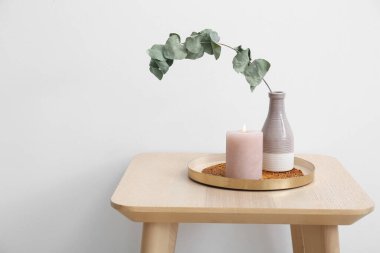 Yanan mum ve vazo, okaliptüs dallarıyla aydınlık duvarın yanındaki masada.