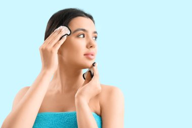 Mavi arka planda pamuk pedlerle makyaj yapan genç bir kadın, yakın plan.